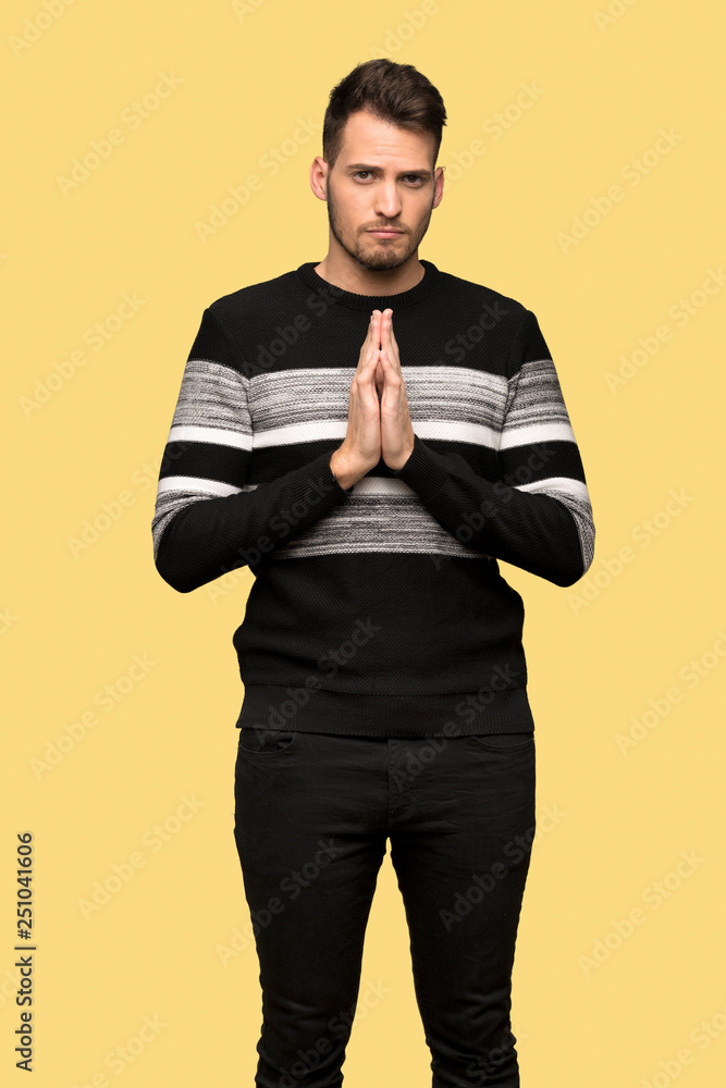 Handsome man keeps palm together. Person asks for something over yellow background Handsome man keeps palm together. Person asks for something over yellow background