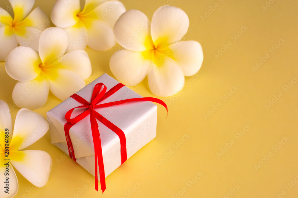White gift box with tropical white flowers (plumeria) on yellow background. Concept for greeting card, postcard. Copy space. White gift box with tropical white flowers (plumeria) on yellow background. Concept for greeting card, postcard. Copy space.