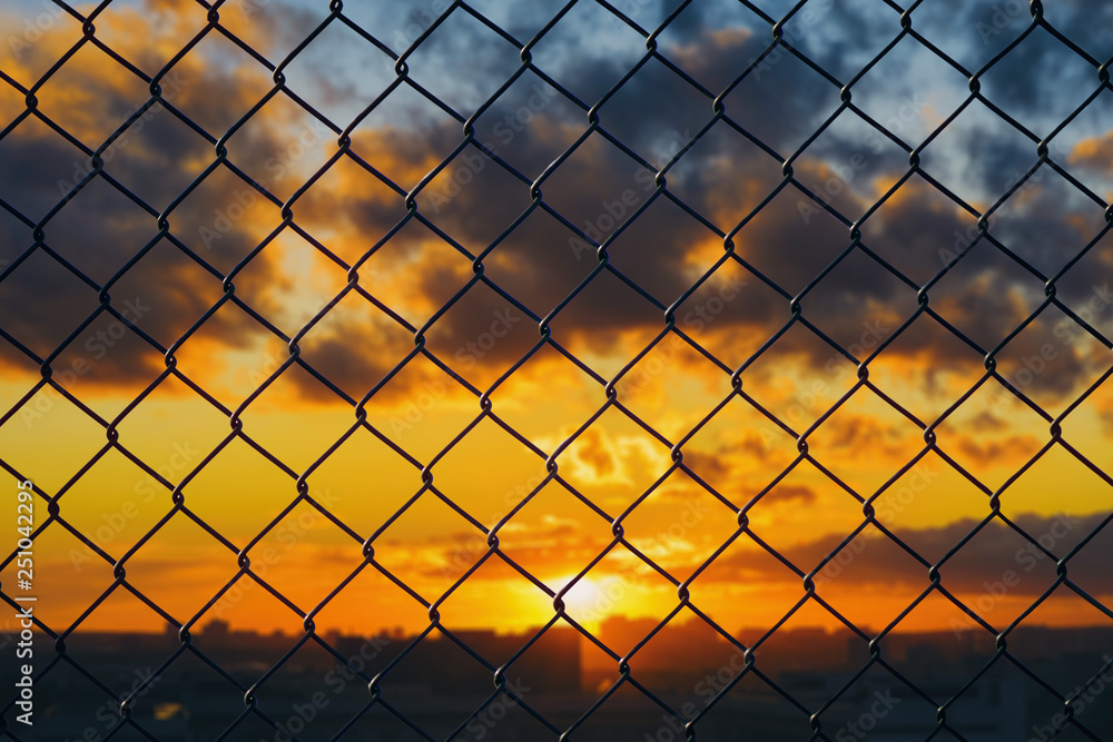 Conceptual image of sunrise sky and steel mesh wire fence. Concept of hope and freedom