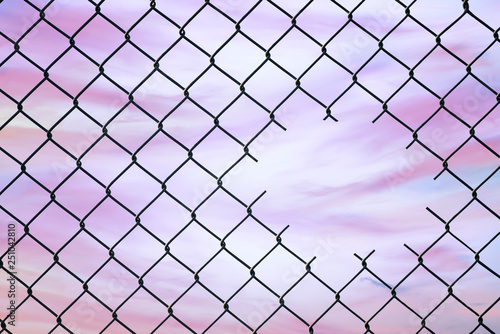 Hole in the center of mesh wire fence on the sky background. Concept of hope and freedom