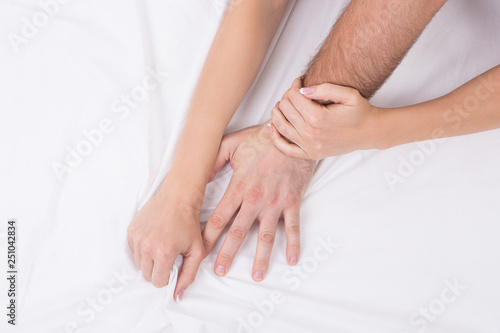 Hands of couple who having sex in bed on white crumpled sheet, focus on hands