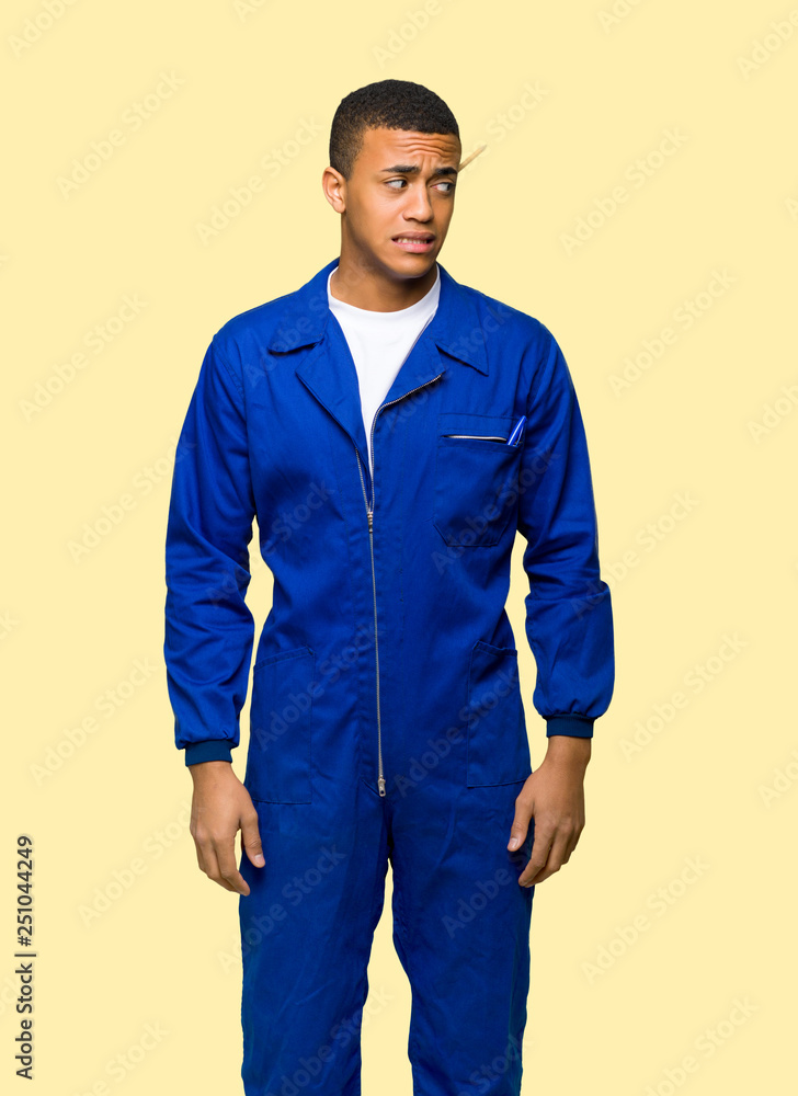 Young afro american worker man is a little bit nervous and scared pressing the teeth on isolated background Young afro american worker man is a little bit nervous and scared pressing the teeth on isolated background