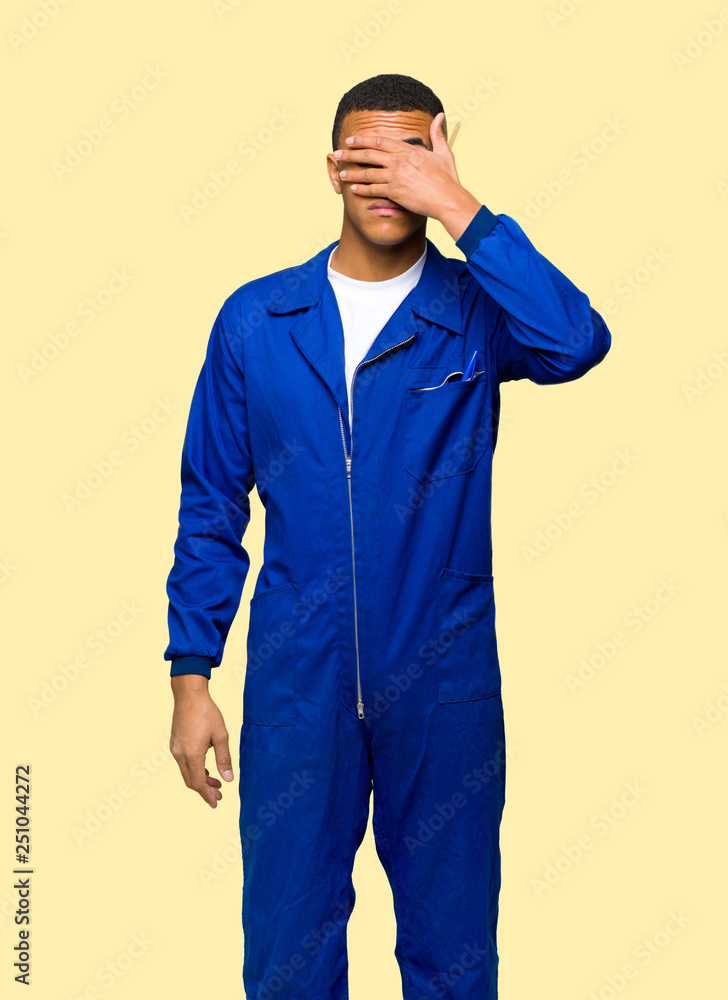 Young afro american worker man covering eyes by hands. Do not want to see something on isolated background Young afro american worker man covering eyes by hands. Do not want to see something on isolated background
