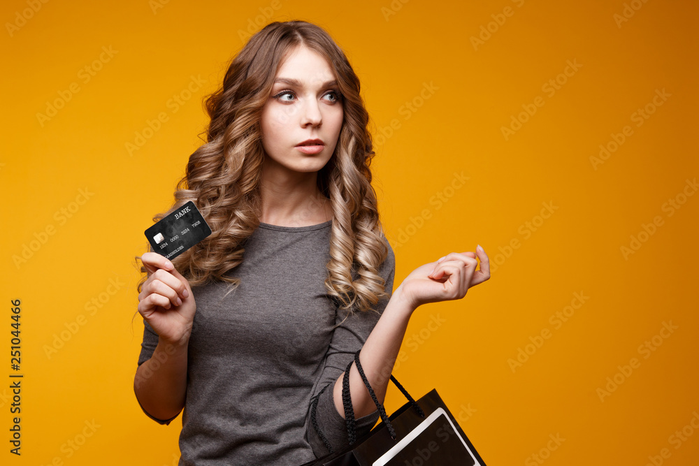 lose-up portrait of happy young brunette woman holding credit card and black shopping bags, looking at camera, isolated on yellow background lose-up portrait of happy young brunette woman holding credit card and black shopping bags, looking at camera, isolated on yellow background