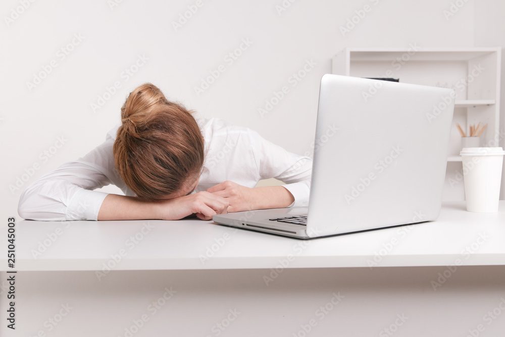 Overworked and tired sleeping over a laptop in a desk at work in her office Overworked and tired sleeping over a laptop in a desk at work in her office