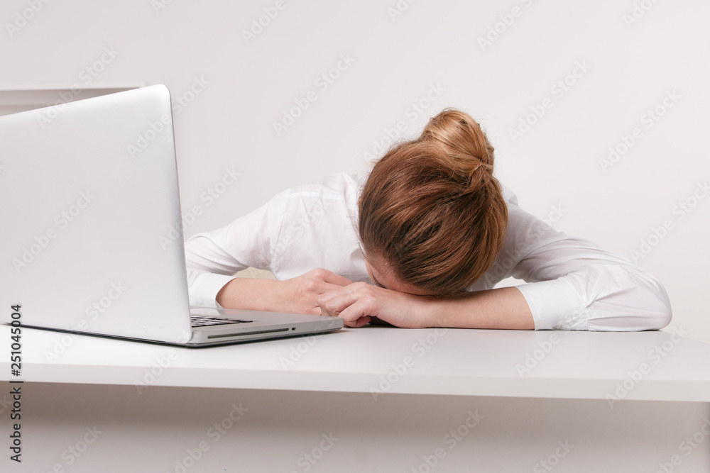 Overworked and tired sleeping over a laptop in a desk at work in her office Overworked and tired sleeping over a laptop in a desk at work in her office