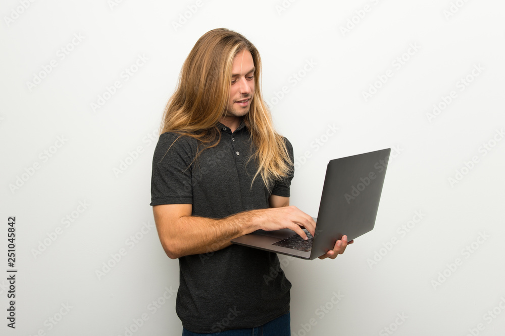 Naklejka premium Blond man with long hair over white wall with laptop