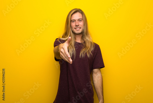 Blond man with long hair over yellow wall shaking hands for closing a good deal © luismolinero