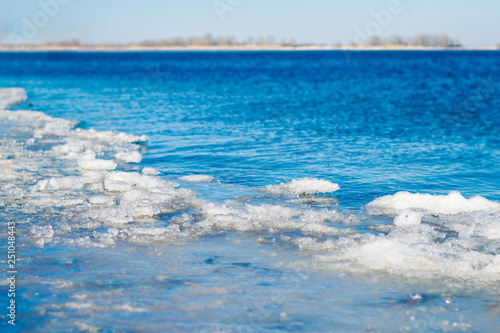 Berih river with remnants of snow and ice. Water is very clean and clear, through it the bottom of the river is visible. Blue water