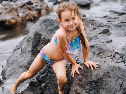 Girl play on a beach in the sea waves and playing on the volcanic sand beach