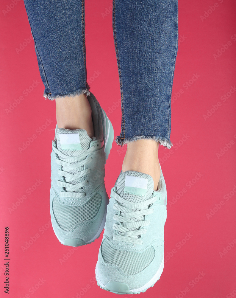 Woman's legs in jeans and black sneakers on red background.