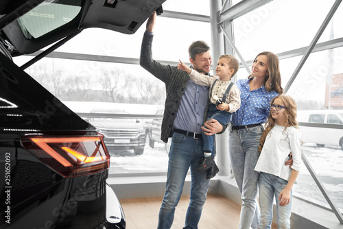 Happy family looking at trunk of expensive black car.