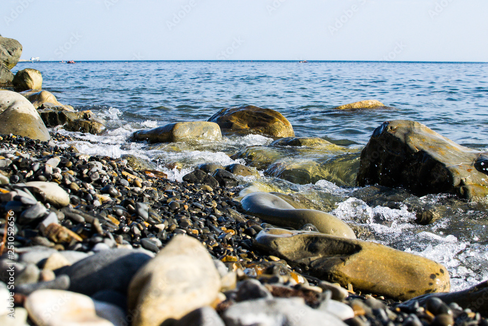 the blue waves crashing against the stones lying on the shore of the black sea and dust flying from them