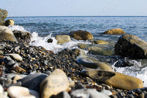 the blue waves crashing against the stones lying on the shore of the black sea and dust flying from them © Павел Чигирь