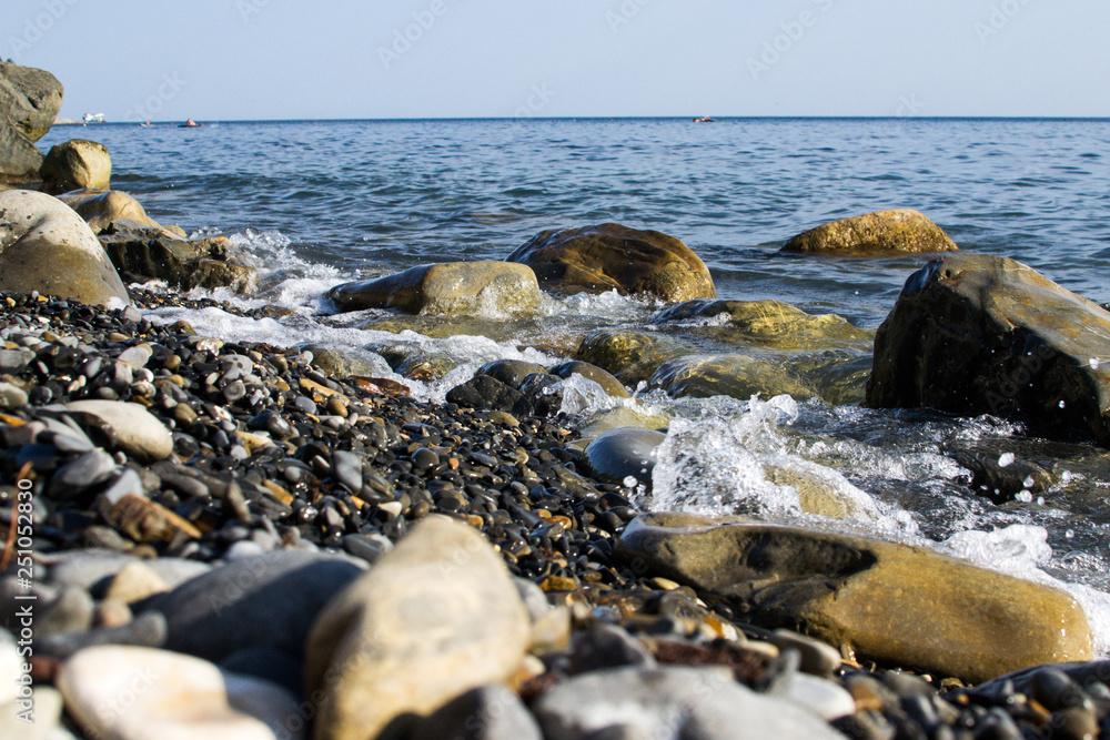 the blue waves crashing against the stones lying on the shore of the black sea and dust flying from them