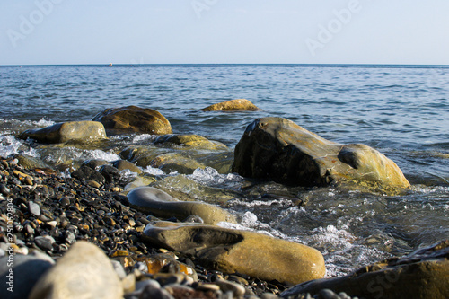 the blue waves crashing against the stones lying on the shore of the black sea and dust flying from them © Павел Чигирь