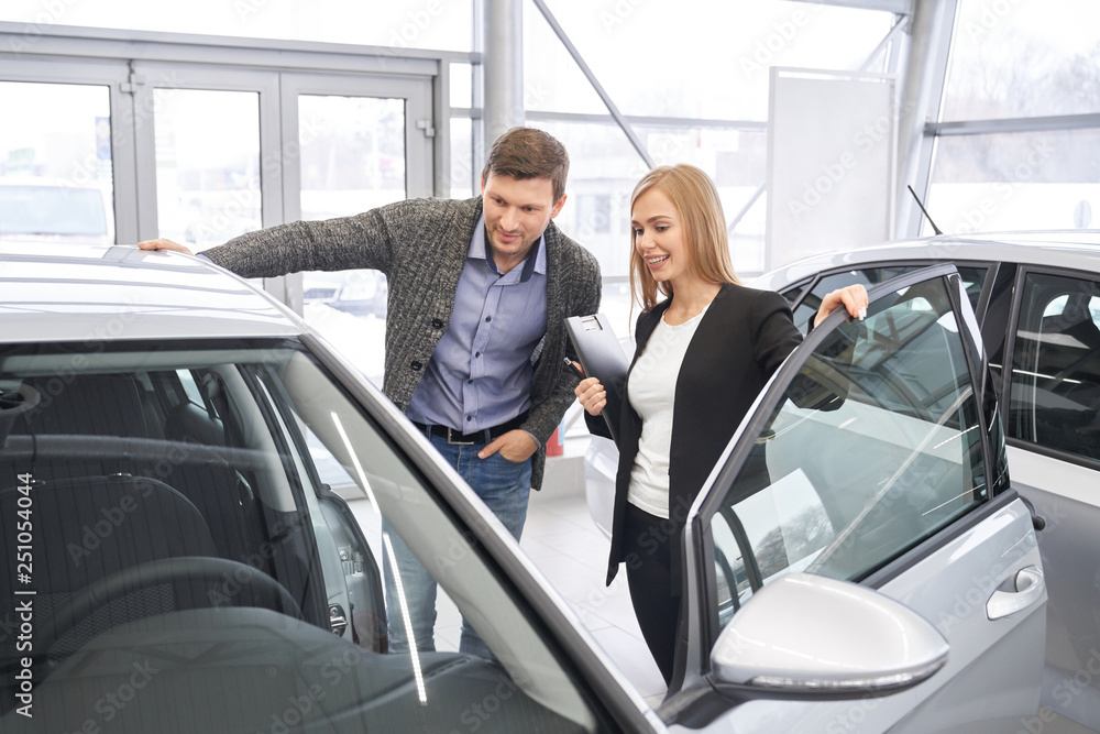 Female car dealer showing automobile to potential buyer.