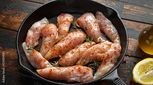 Raw chicken breast mini fillets in rastic cast iron skillet, frying pan with herbs and sea salt