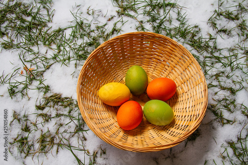 Five colorful easter eggs in a straw basket on top of snow and grass isolated egg hunt