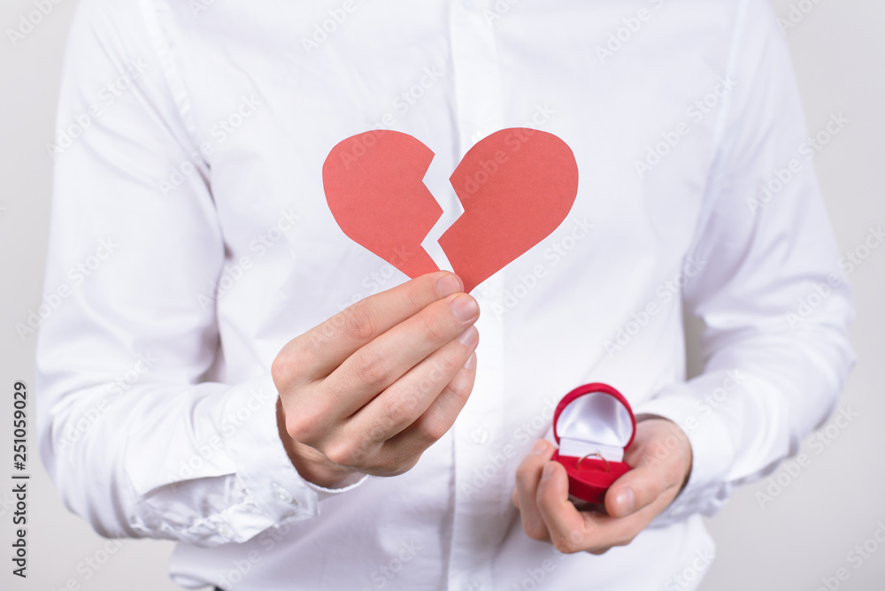 No date concept. Cropped closeup photo of confused unhappy sad guy holding showing broken heart in hand isolated grey background No date concept. Cropped closeup photo of confused unhappy sad guy holding showing broken heart in hand isolated grey background