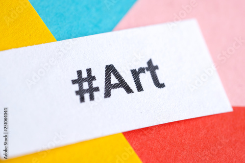 Popular hashtag 'art' printed on white sheet of paper on a multicolored background. Close up.