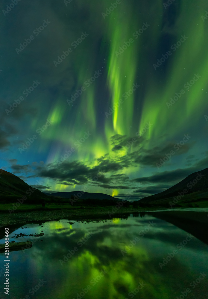 aurora borealis in the night sky cut the mountains, reflected in the water.