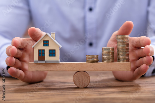 House Model And Golden Coins Balancing On Seesaw photo