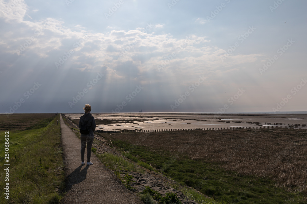 Fototapeta premium Person geht dem Licht entgegen auf dem Trischendamm in Friedrichskoog Spitze
