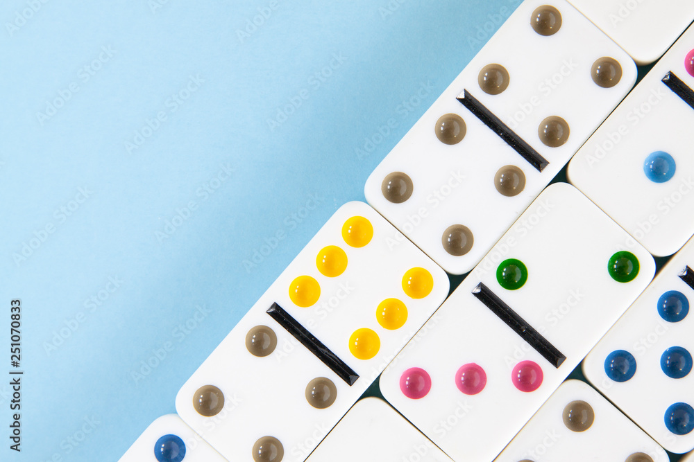 Overhead closeup of white dominoes with brightly colored dots on a blue background with copy space Overhead closeup of white dominoes with brightly colored dots on a blue background with copy space