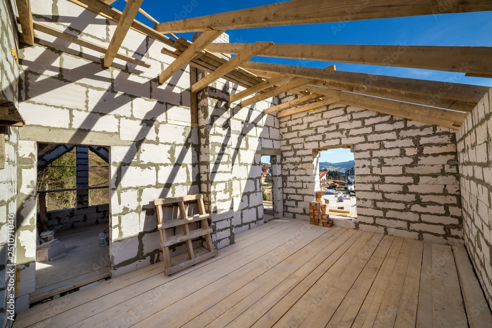 House interior under construction and renovation. Energy saving walls of hollow foam insulation blocks and bricks, ceiling beams and roof frame.