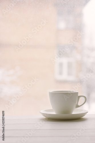 White cup in window sill on a background of house and snowy weather.