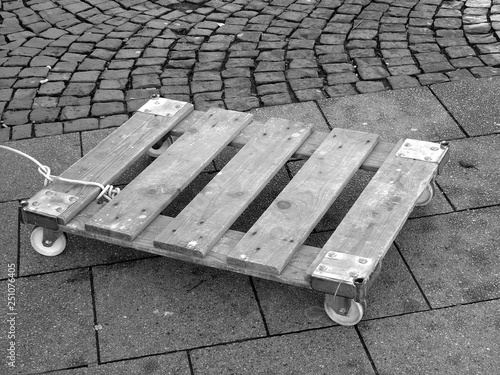 Alte Holzpalette auf Rollen zum Transport schwerer Gegenstände auf Kopfsteinpflaster am Wochenmarkt im Stadtteil Bockenheim in Frankfurt am Main in Hessen, fotografiert in klassischem Schwarzweiß photo