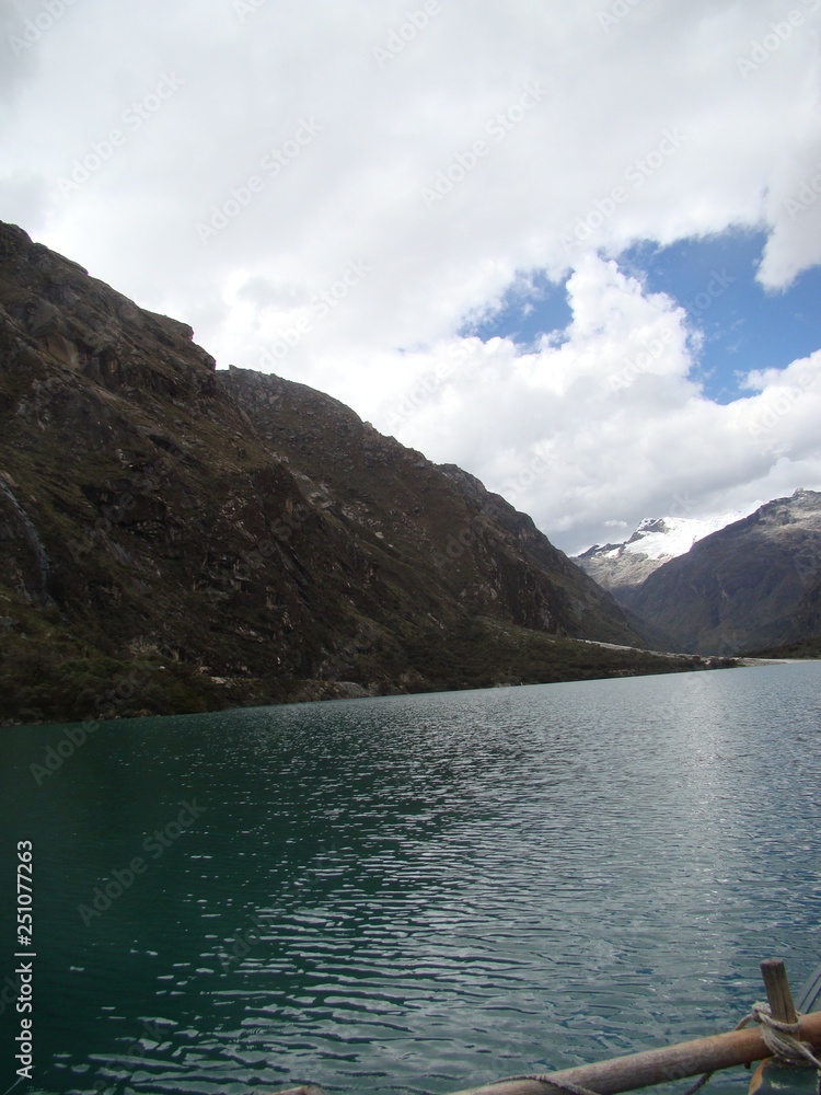 Mountain with snow on top and a turquoise lake below, blue sky with clouds