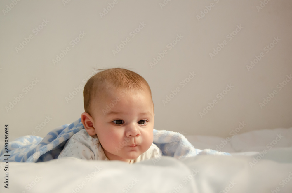 cute 4 months old baby boy having tummy time on white quilt covered with blue blanket cute 4 months old baby boy having tummy time on white quilt covered with blue blanket