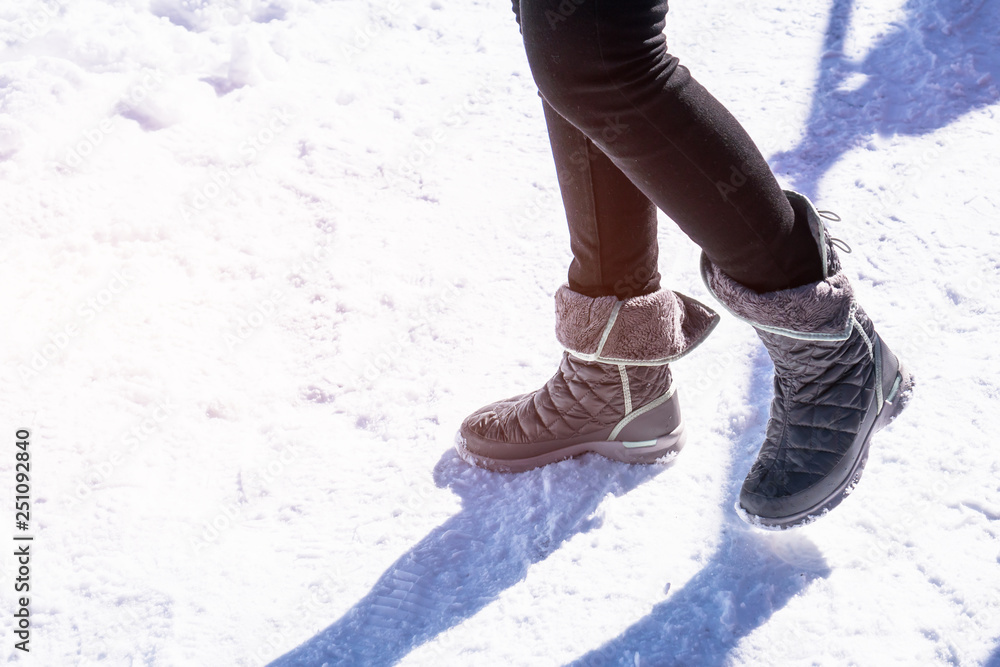 Woman boots walking on snow road in fresh nature park in cold season, Closeup of winter shoes of snowy with flare light in sunny day Woman boots walking on snow road in fresh nature park in cold season, Closeup of winter shoes of snowy with flare light in sunny day