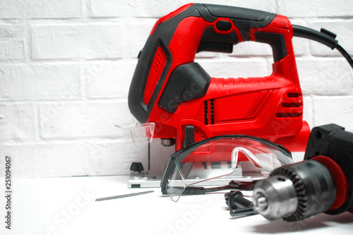 Professional building electrical tools for wood and metal. Electric jig saw and drill with safety glasses on a brick wall background.