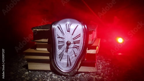 Time Concept. Distorted soft melting clock on a old books, the Persistence of Memory of Salvador Dali. With dark toned foggy background. Selective focus