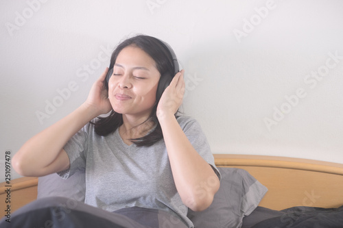 beautiful Asian woman listening music with headphone relaxing on the bed