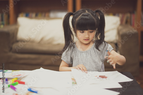 Portrait of cute little girl create art on paper with colored paint on the table at home. Concept of education.