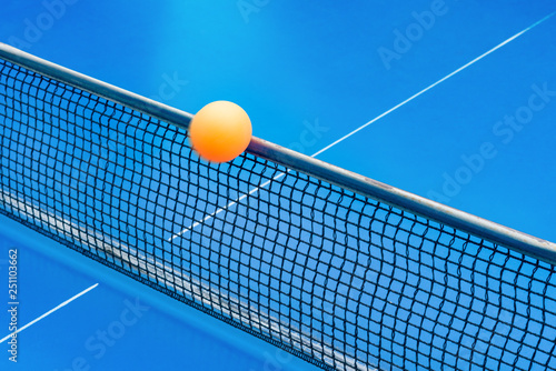 yellow ball hits the netting on a blue pingpong table © Freer