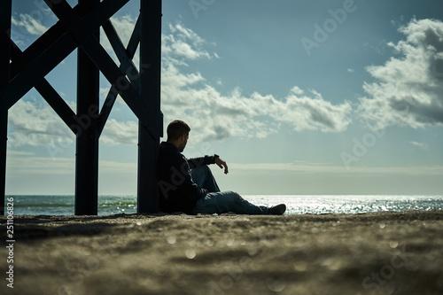 Fototapeta silueta hombre vestido sentado en la playa mirando al mar