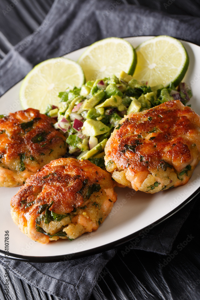 Freshly made salmon burgers with avocado salsa and lime close-up on a plate. vertical Freshly made salmon burgers with avocado salsa and lime close-up on a plate. vertical