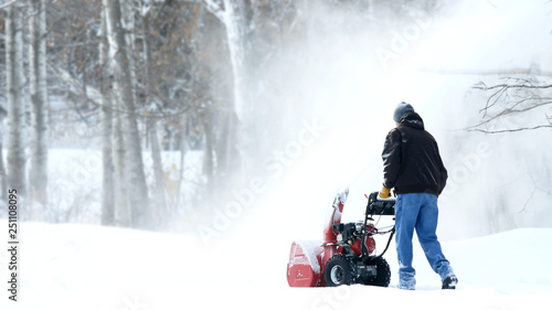 Man works with a snow blower to remove newly fallen snow from driveway after storm in Minnesota.