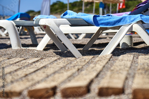 Beach loungers with blue towels. Pebbles covering old pallet walkway