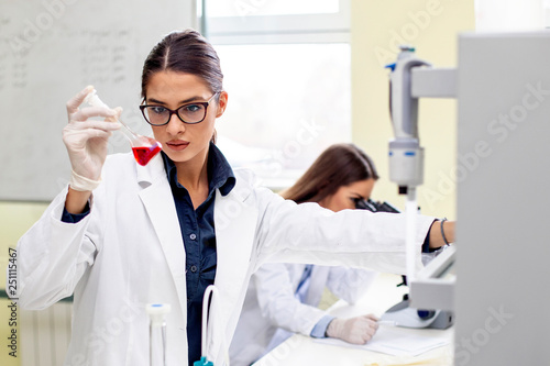 Young woman analyze while second looking at microscope in background