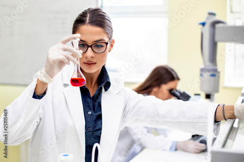 Young woman analyze while second looking at microscope in background
