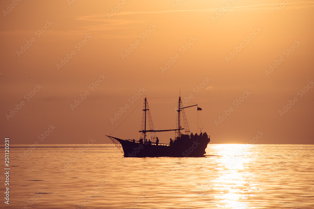 Silhouette of an old ship with masts and people on a bright background of the sea landscape.