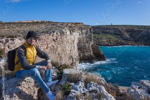 man tourist in yellow vest with backpack on rock cliff in Malta