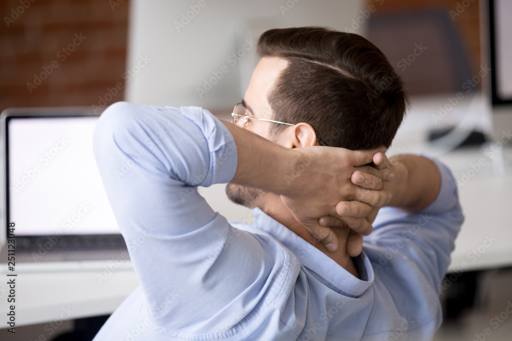 Worker sitting at desk holds hands behind head resting indoors Worker sitting at desk holds hands behind head resting indoors