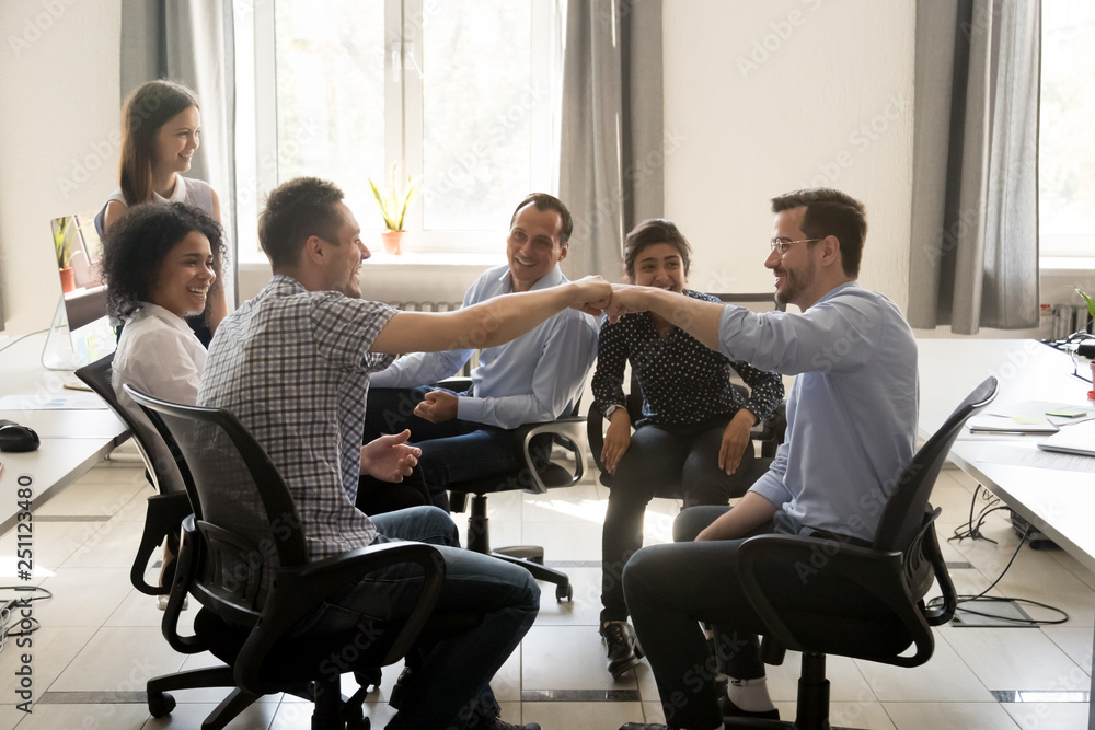 Colleagues fist bumping communicating sitting in coworking area Colleagues fist bumping communicating sitting in coworking area